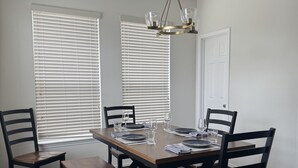 Uma sala de jantar com mesa de madeira, quatro cadeiras e um lustre.