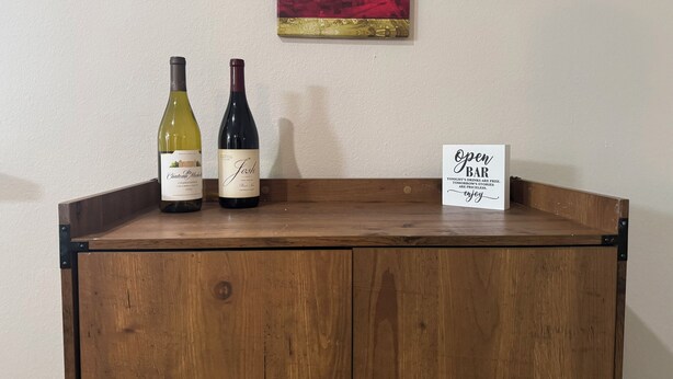 Armário de madeira com duas garrafas de vinho e uma placa indicando um bar.