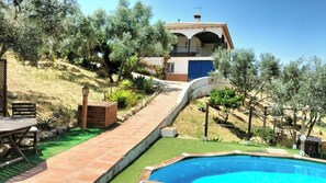 A pool area with a patio, a wooden deck, and a house with a blue door. - Casa Pil Riogordo by Ruralidays (Málaga)