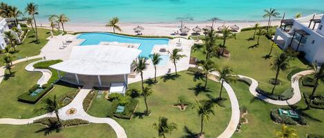 A resort with a central swimming pool, palm trees, and a beach view.