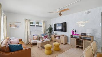Een moderne woonkamer met een bank, fauteuil, salontafel, poefjes, televisie en een decoratieve wand.