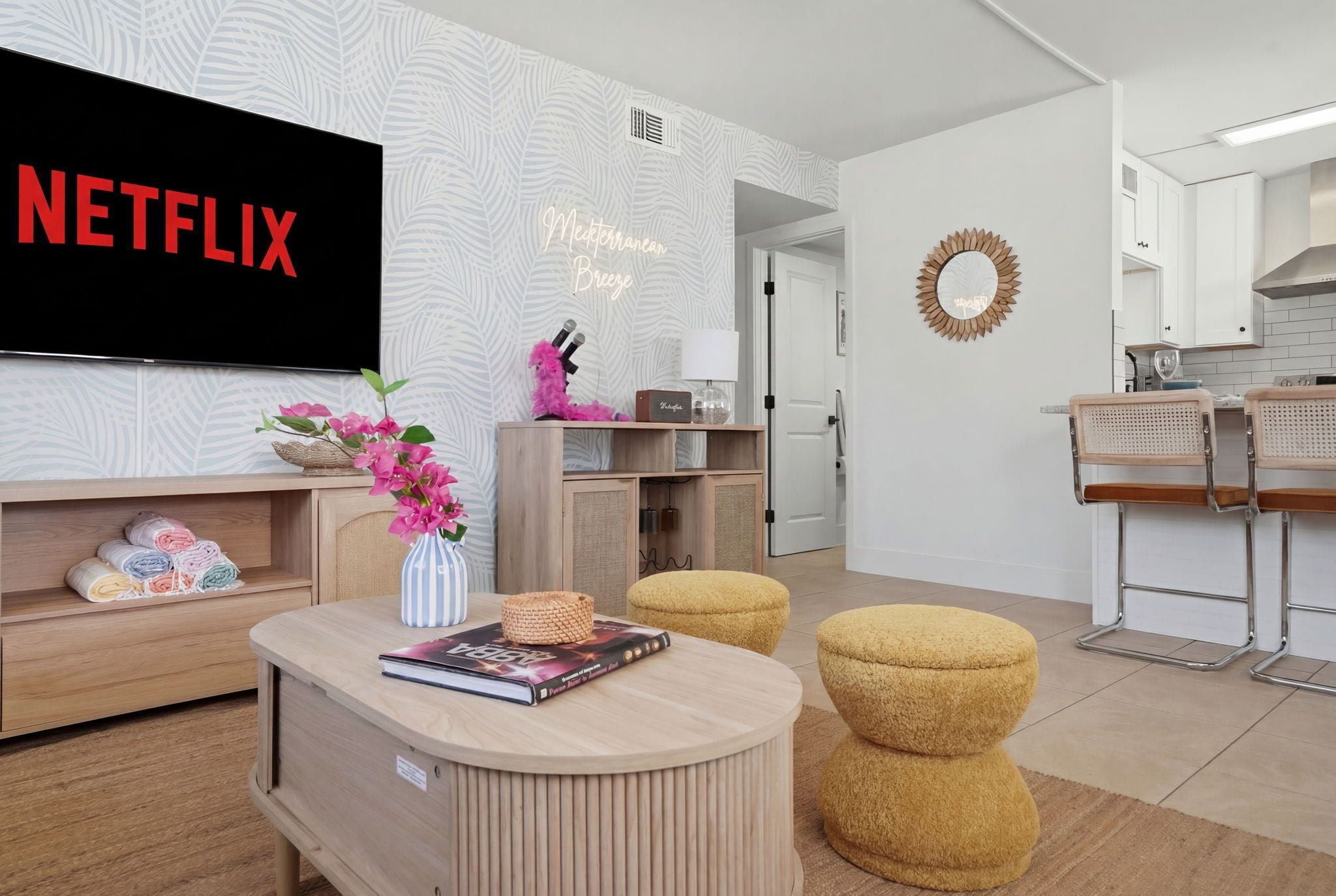A modern living room with a flat-screen TV, a bookshelf, a coffee table, and a kitchen area in the background.