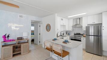 A modern kitchen with white cabinets, a stainless steel refrigerator, and a central island with bar stools.