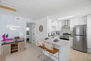 Een moderne keuken met witte kasten, een roestvrijstalen koelkast en een centraal eiland met barkrukken.