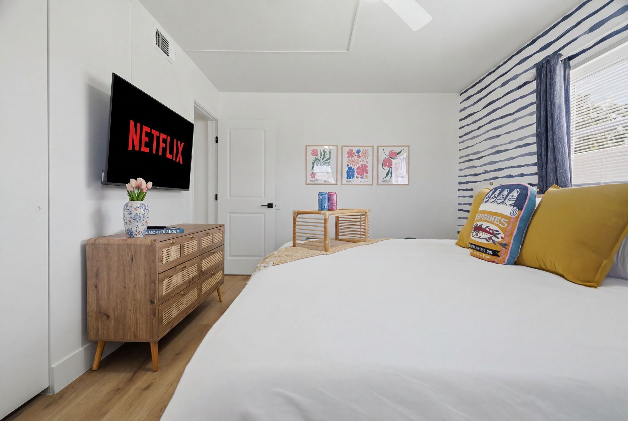 A bedroom with a bed, a wooden dresser, a television displaying 'NETFLIX', and wall art.