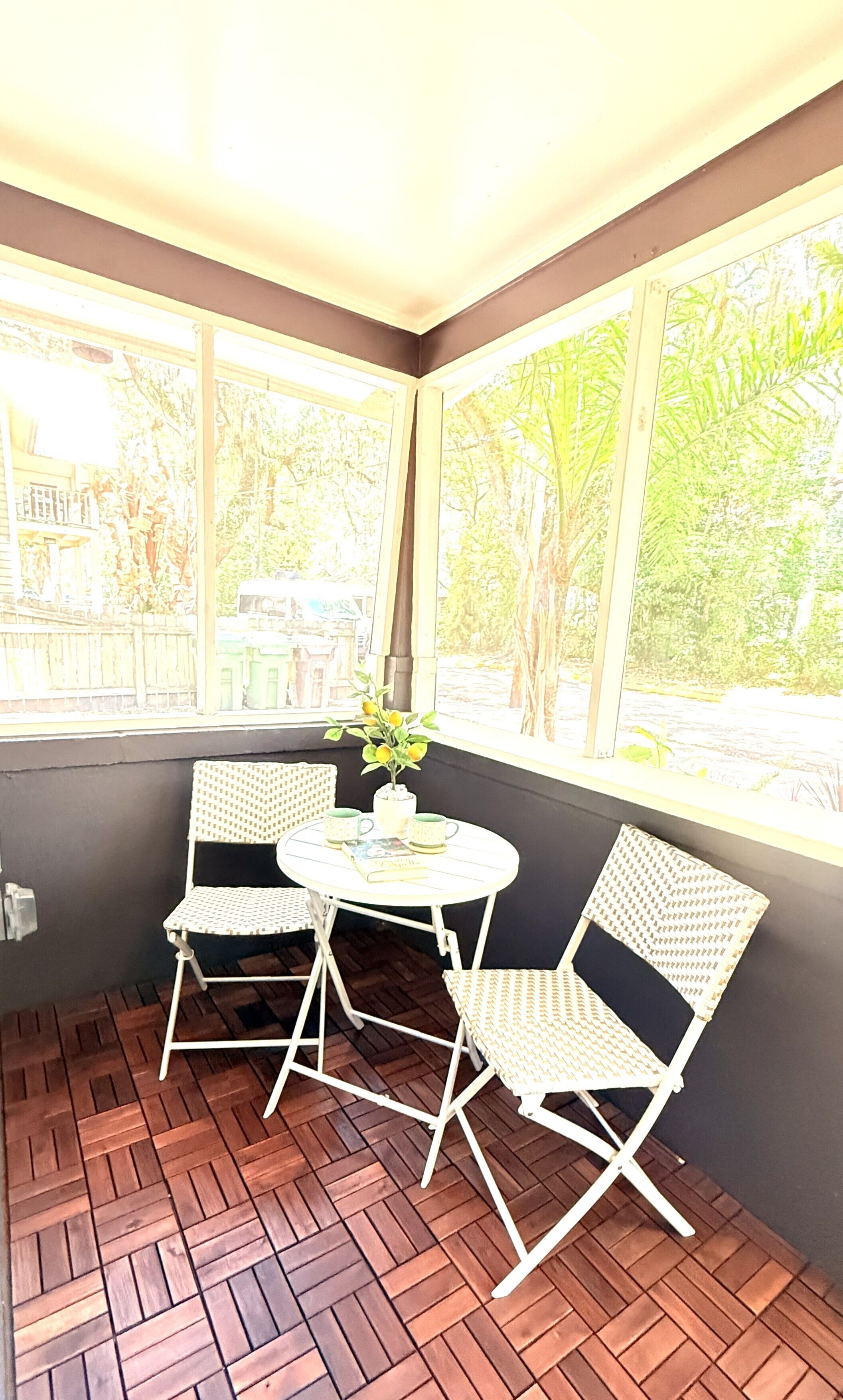 Habitación de esquina con una pequeña mesa y dos sillas, una ventana con vistas a zonas verdes, y un suelo con diseño.