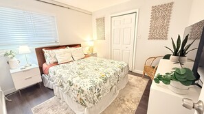 Ein Schlafzimmer mit Bett, Nachttisch, Lampe, Topfpflanzen und einer Tür.