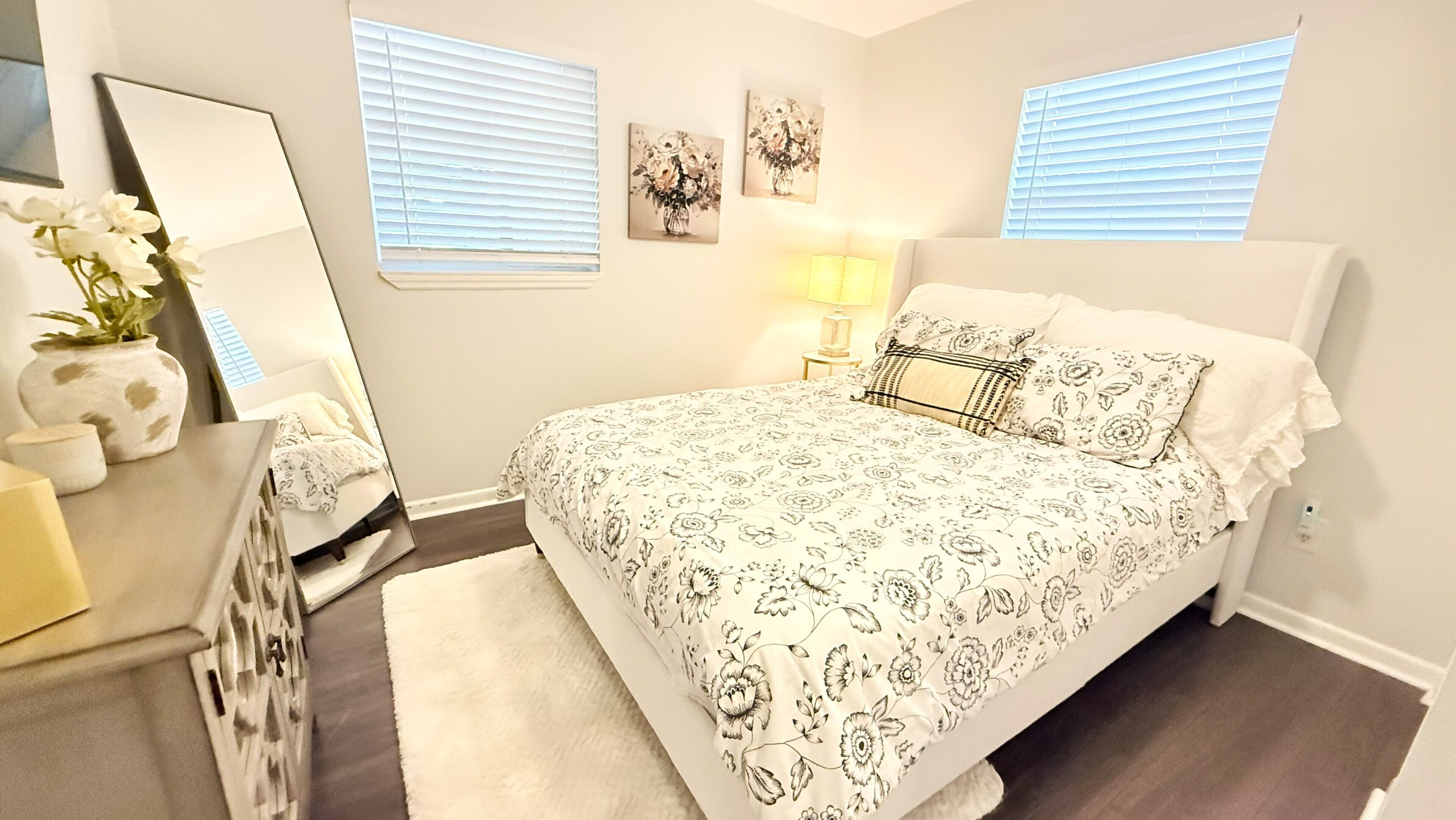 A bedroom with a bed, bedside tables, a mirror, and wall art.