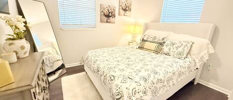 A bedroom with a bed, bedside tables, a mirror, and wall art.