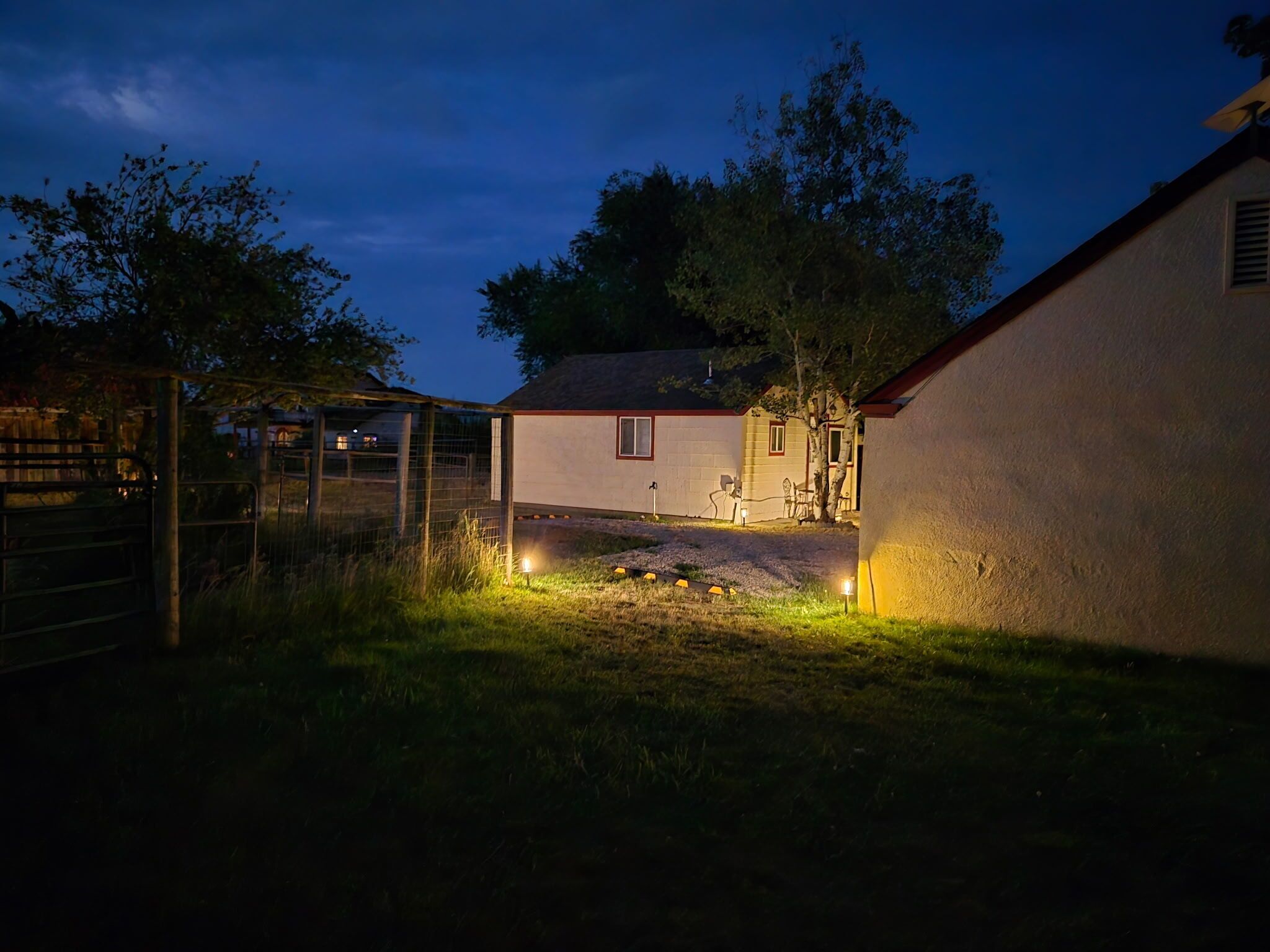 A fenced outdoor area with a building, a tree, and a well-lit path.