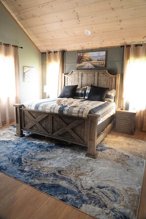 Quarto com cama de madeira, cabeceira, mesa de cabeceira, pintura e janela com cortinas.