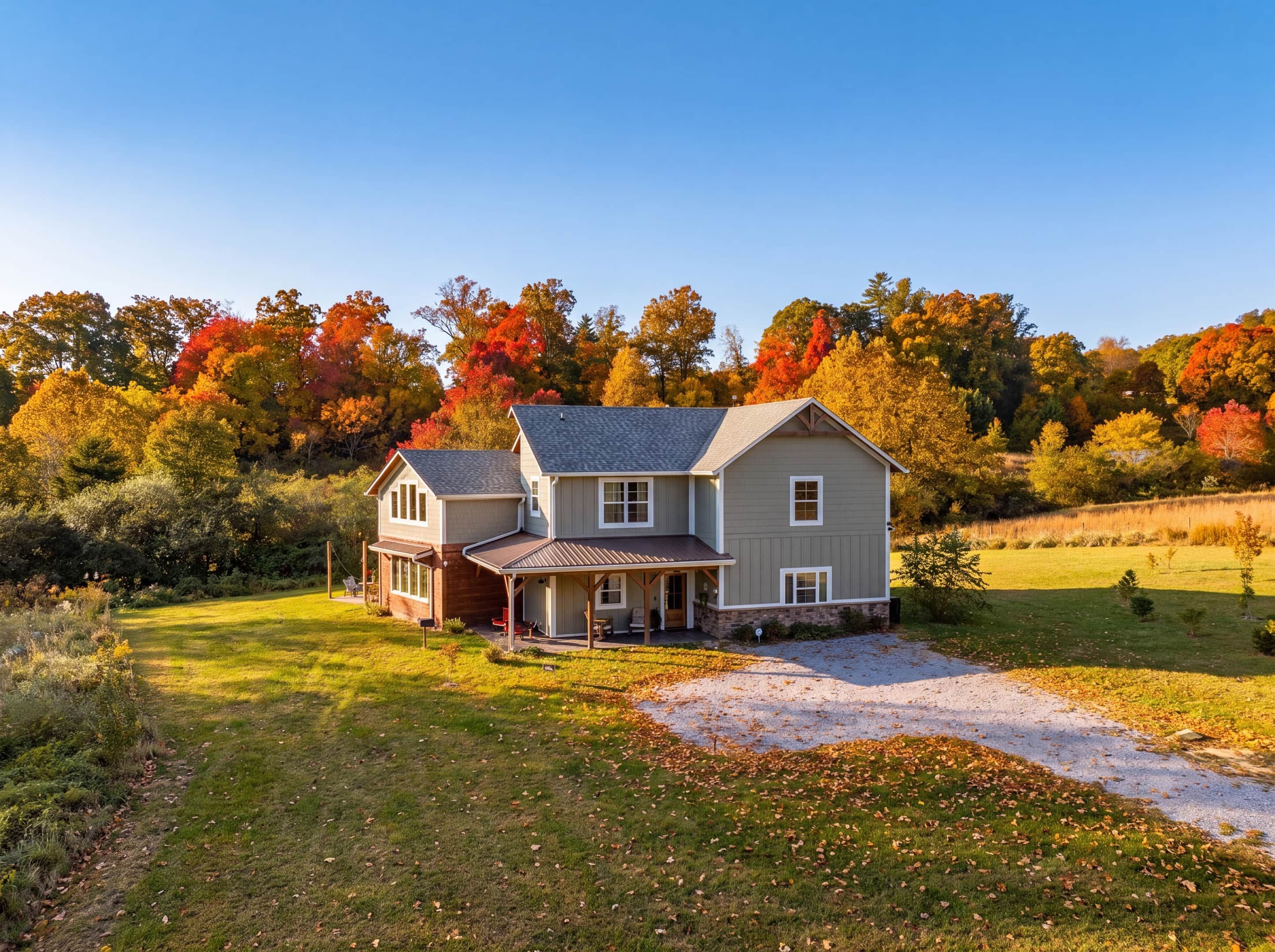 A two-story house with a porch, surrounded by a grassy yard and trees with autumn foliage.
