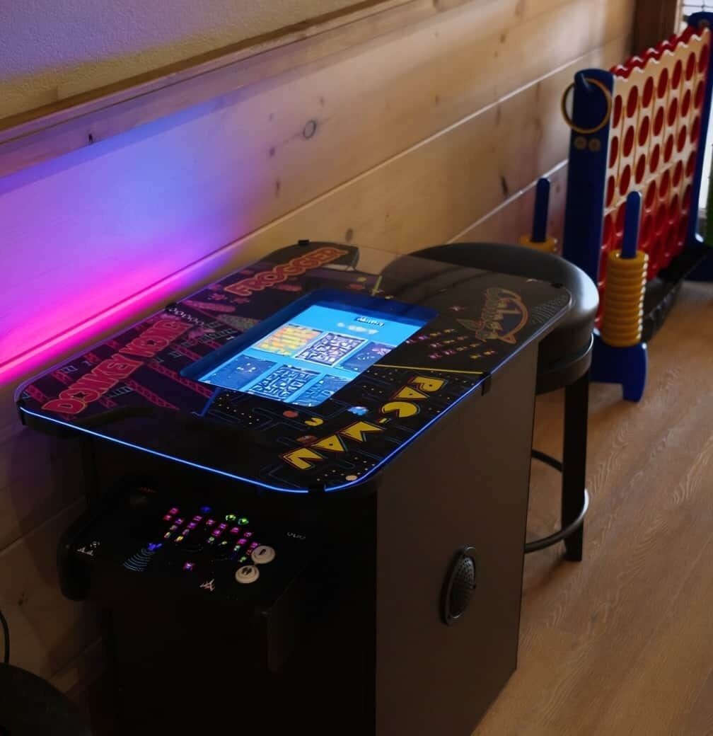 Una consola de videojuegos con pantalla y botones de colores, sobre un piso de madera y un radiador al fondo.