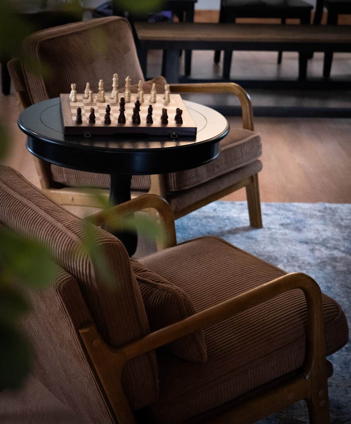 A chessboard on a table with a chair in the foreground.