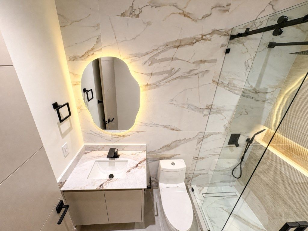 A modern bathroom with a marble vanity, a toilet, and a glass-enclosed shower.