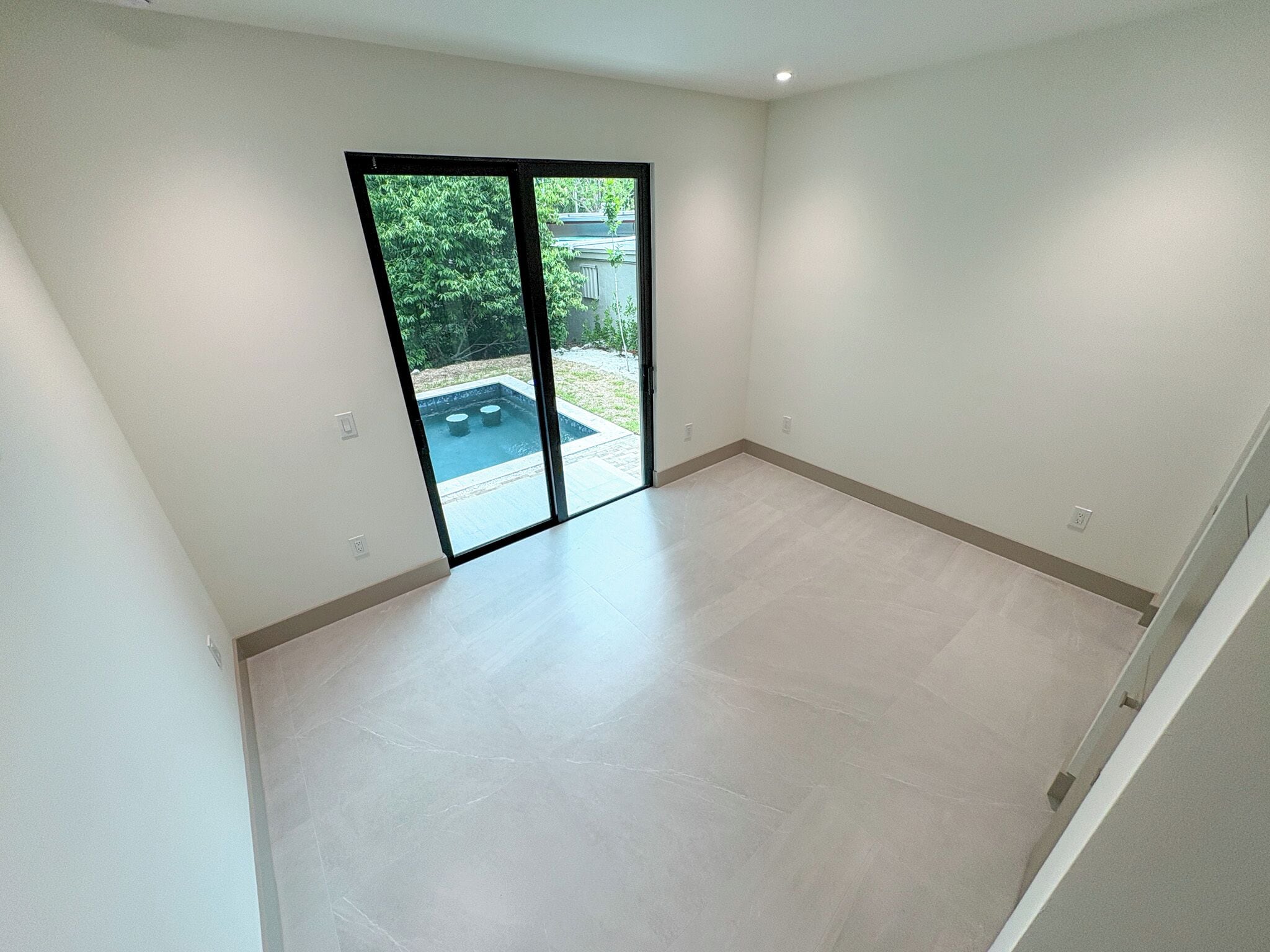 A spacious room with a large sliding glass door leading to an outdoor area with a swimming pool.