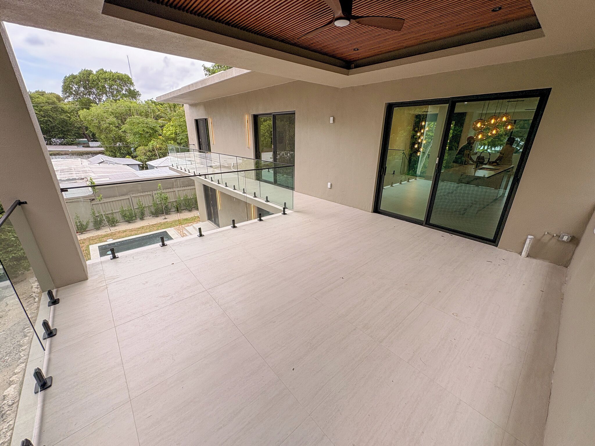 A spacious balcony with a glass railing overlooking a garden and a building with solar panels.