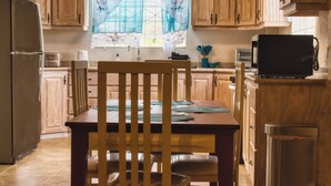 Et køkken med træskabe, et spisebord med stole, et køleskab og en mikrobølgeovn.
