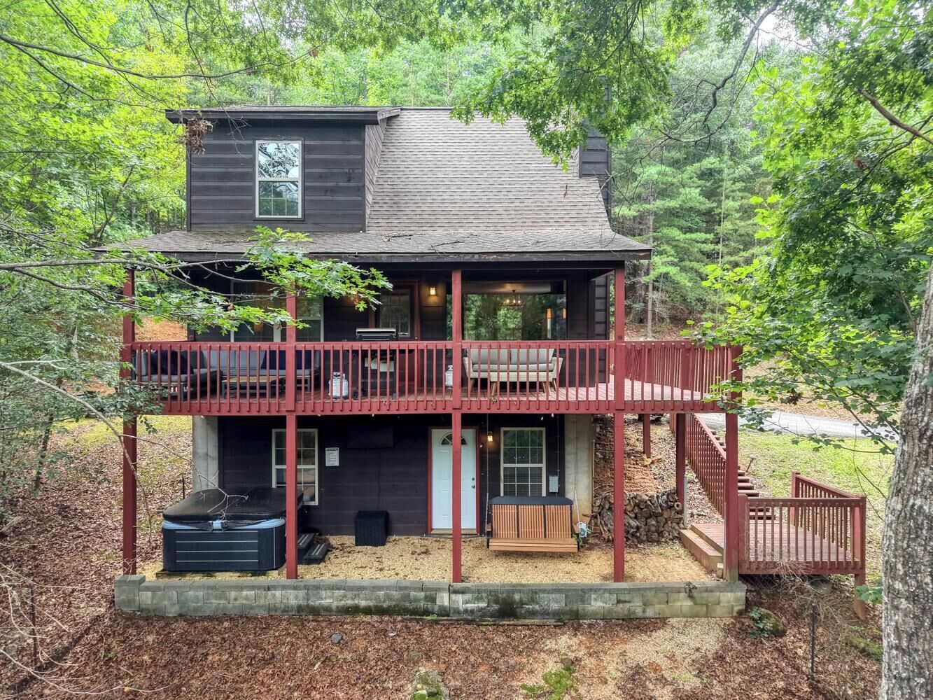 A two-story cabin with a balcony, a hot tub, and a deck.