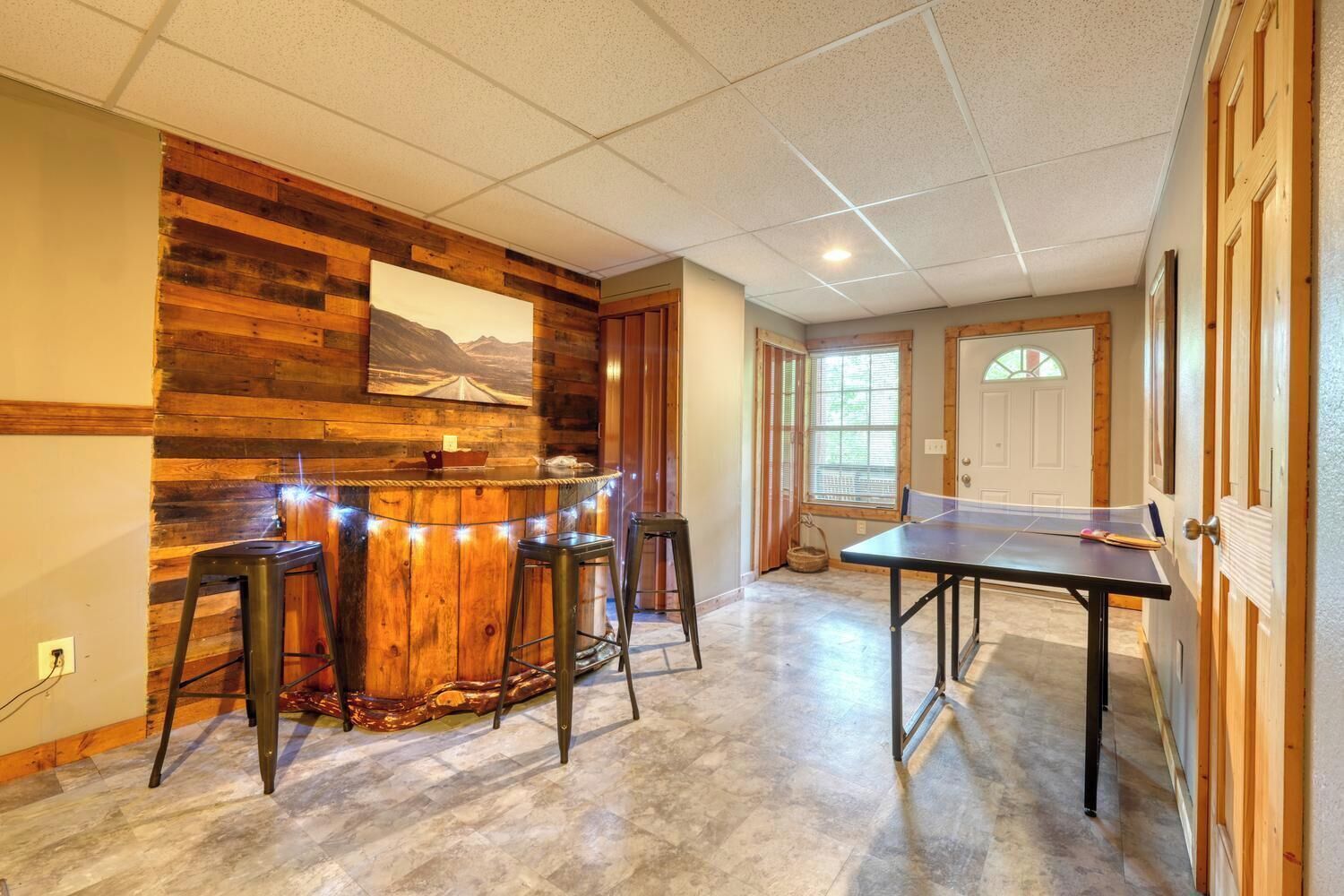 A room with a ping pong table, wooden bar counter, and two stools.