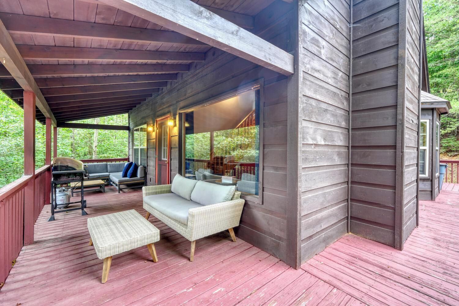 A covered outdoor area with a wooden deck, a sofa, and a grill.