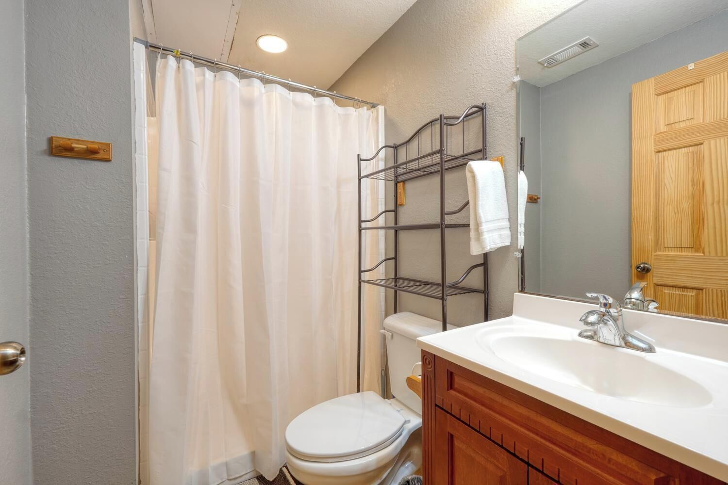 A bathroom with a shower curtain, a toilet, a sink with a mirror, and a wooden cabinet.