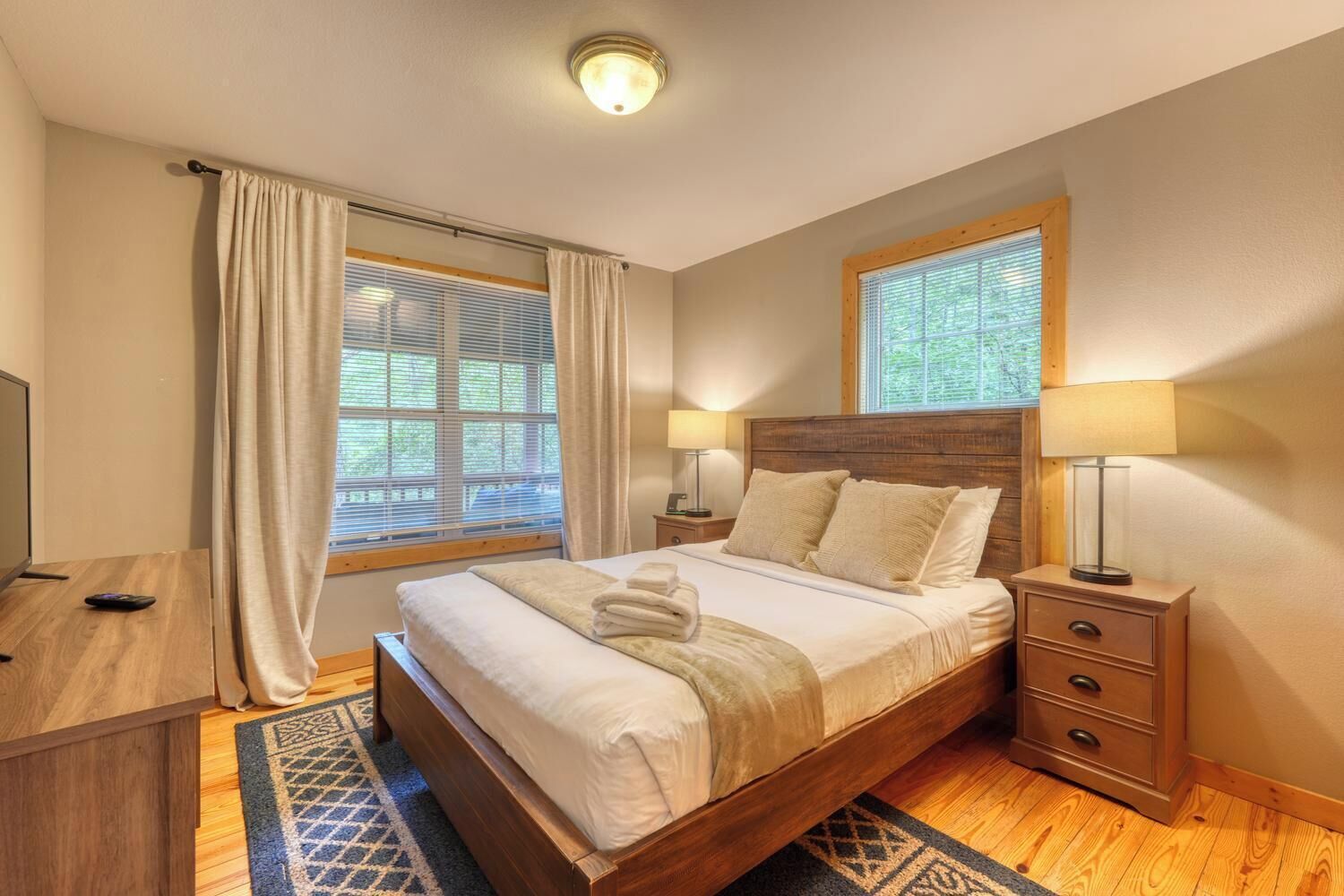 Un dormitorio con una cama de madera, dos mesitas de noche, un escritorio y una ventana con cortinas.