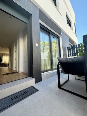 A modern building entrance with a sliding glass door, a black outdoor chair, and a 'HOME' mat. - Viktoriia's Home in Orihuela (Orihuela)