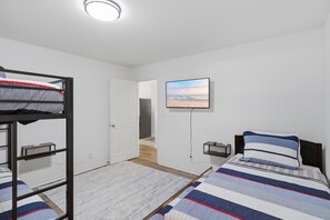 Ein Zimmer mit Etagenbetten, einem Flachbildfernseher an der Wand und einer Tür zu einem weiteren Raum.