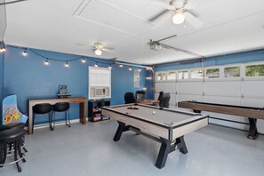 A recreational room with a pool table, two pool tables, ceiling fans, string lights, and a window with blinds. - Waterfront|Sleeps10|GameRoom|Covered Patio|PetsOk (Lake Ozark)