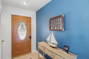 Eine Holztür mit einem Buntglasfenster, einem an der Wand befestigten Schlüsselhalter, einem Modellsegelschiff und einem WLAN-Symbol auf einer Holztischplatte.