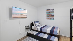 Ein Schlafzimmer mit einem Bett, einem an der Wand montierten Fernseher und einem Poster mit verschiedenen Freizeitaktivitäten.