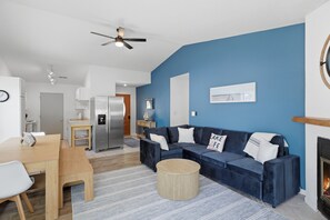 Ein modernes Wohnzimmer mit blauer Akzentwand, einem dunkelblauen Sofa, einem Holztisch und einem Kamin.