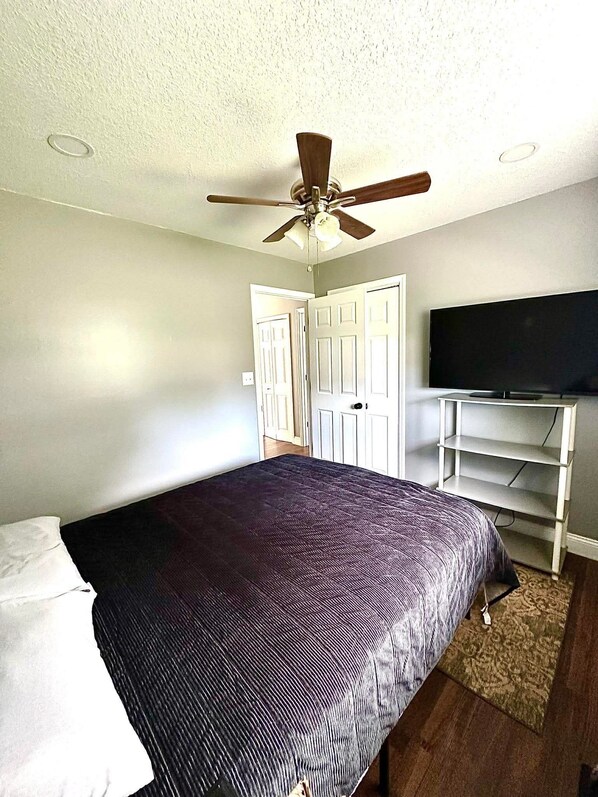 A bedroom with a bed, a ceiling fan, a TV on a stand, and a door.