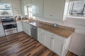 Una cocina con armarios blancos, encimera de granito, electrodomésticos de acero inoxidable y una ventana con persianas.