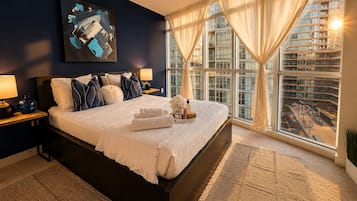 Un dormitorio moderno de hotel con una cama grande, vistas a la ciudad y un cuadro en la pared.
