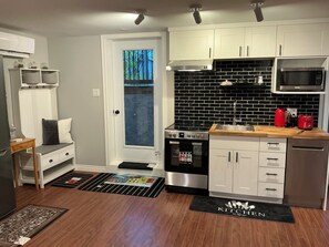 A modern kitchen with white cabinets, a black tiled backsplash, stainless steel appliances, and a wooden countertop.
