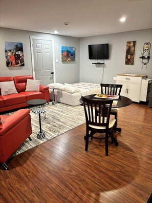 A living room with a red sofa, a dining table with chairs, a TV mounted on the wall, and artwork on the walls.