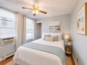 A bedroom with a bed, a ceiling fan, a window with blinds, a bedside lamp, and a wall-mounted picture. - Walk To The Beach | Cozy Getaway (Old Orchard Beach)