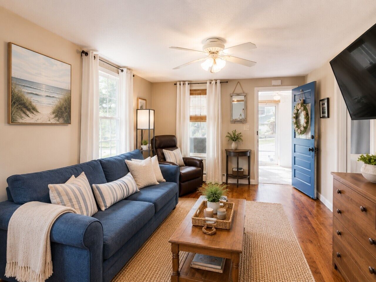 A living room with a blue sofa, a wooden coffee table, a ceiling fan, and a door leading outside.