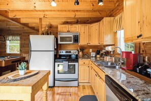 A wooden cabin kitchen with a refrigerator, stove, microwave, and sink.