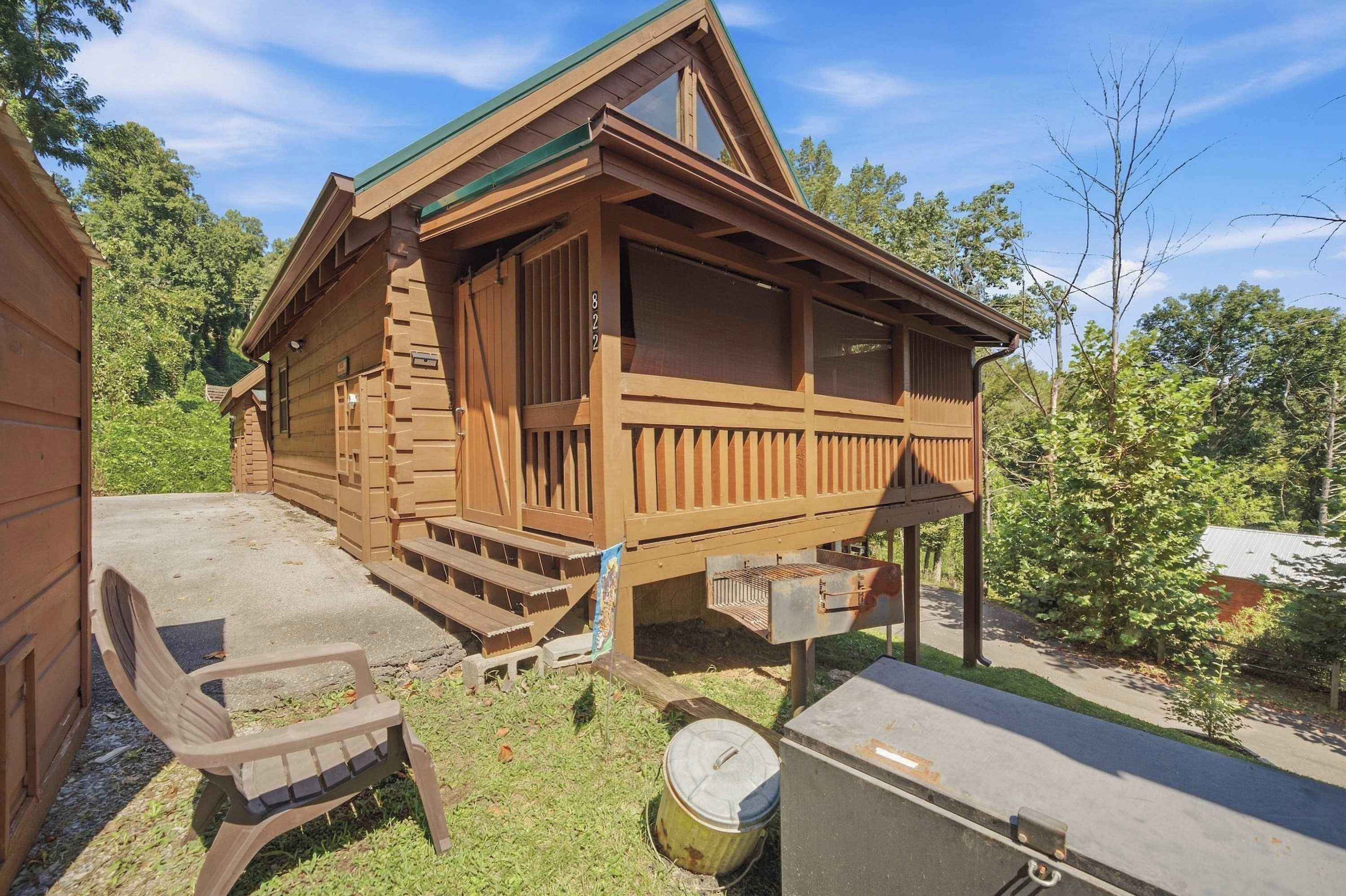 A wooden cabin with a porch, a small attached garage, and a picnic table.