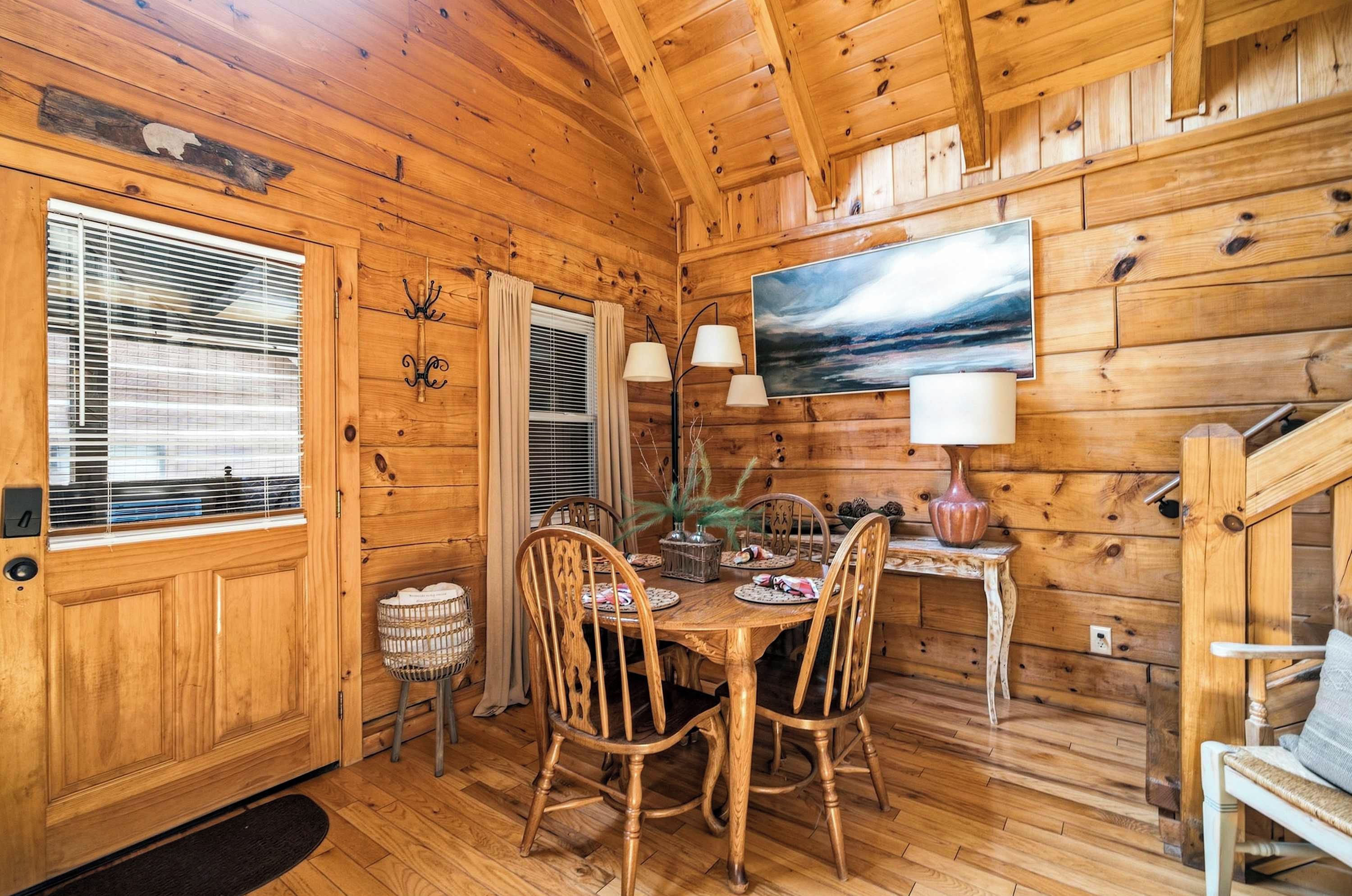 L’intérieur d’un chalet en bois, avec une table à manger, des chaises, un tableau et un escalier.