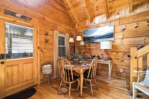 A wooden cabin interior with a dining table, chairs, a painting, and a staircase. - Best Location - Cozy Log Cabin - Hot Tub & Pool (Gatlinburg)