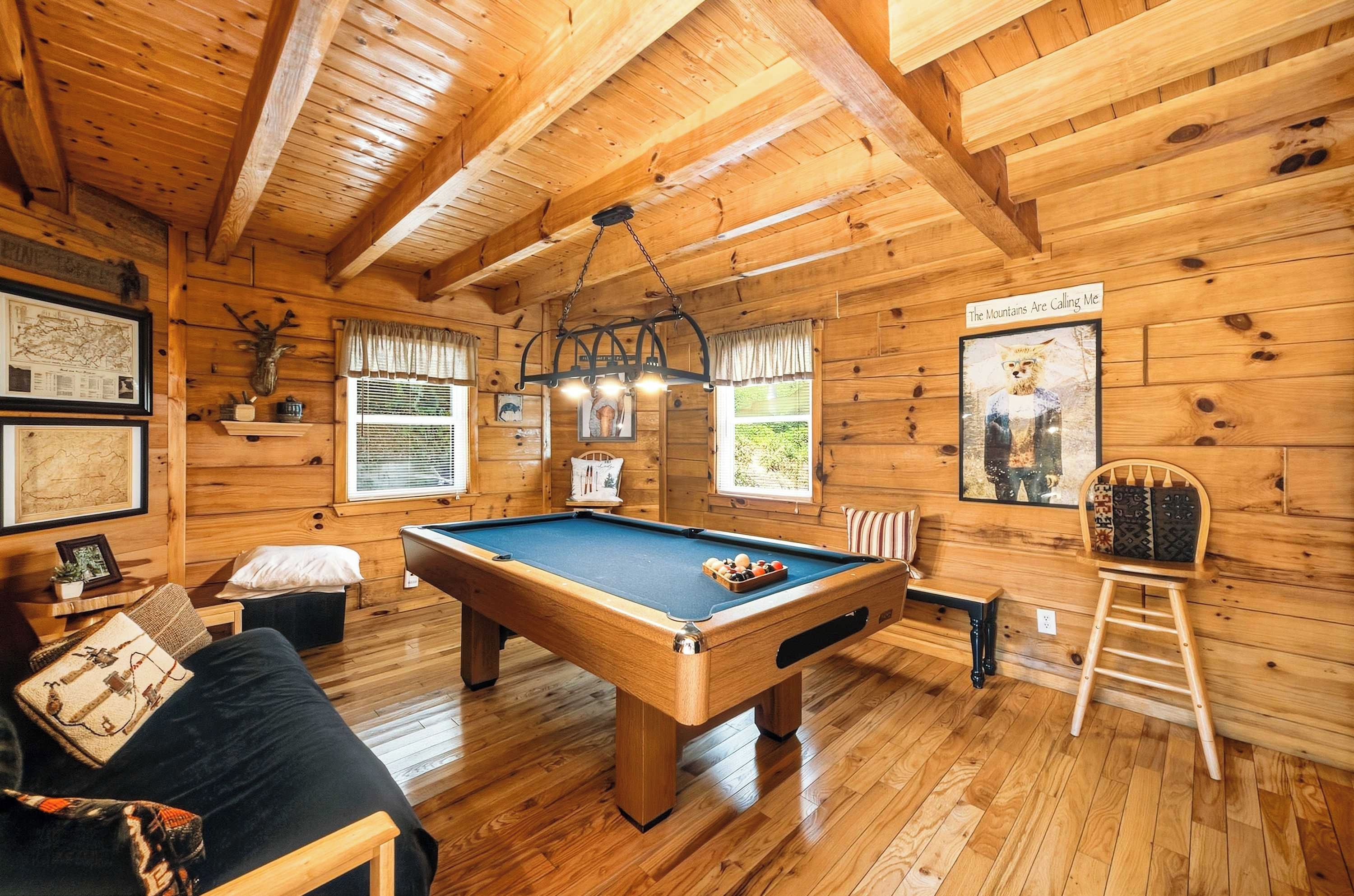 L'intérieur d'un chalet en bois, avec une table de billard, un canapé et un fauteuil.