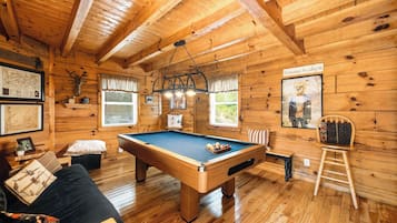 L'intérieur d'un chalet en bois, avec une table de billard, un canapé et un fauteuil.