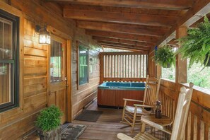 A wooden cabin with a hot tub, wooden chairs, and a door with a window.