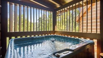 A hot tub with a wooden deck and railings, surrounded by trees.