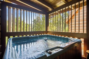 A hot tub with a wooden deck and railings, surrounded by trees.