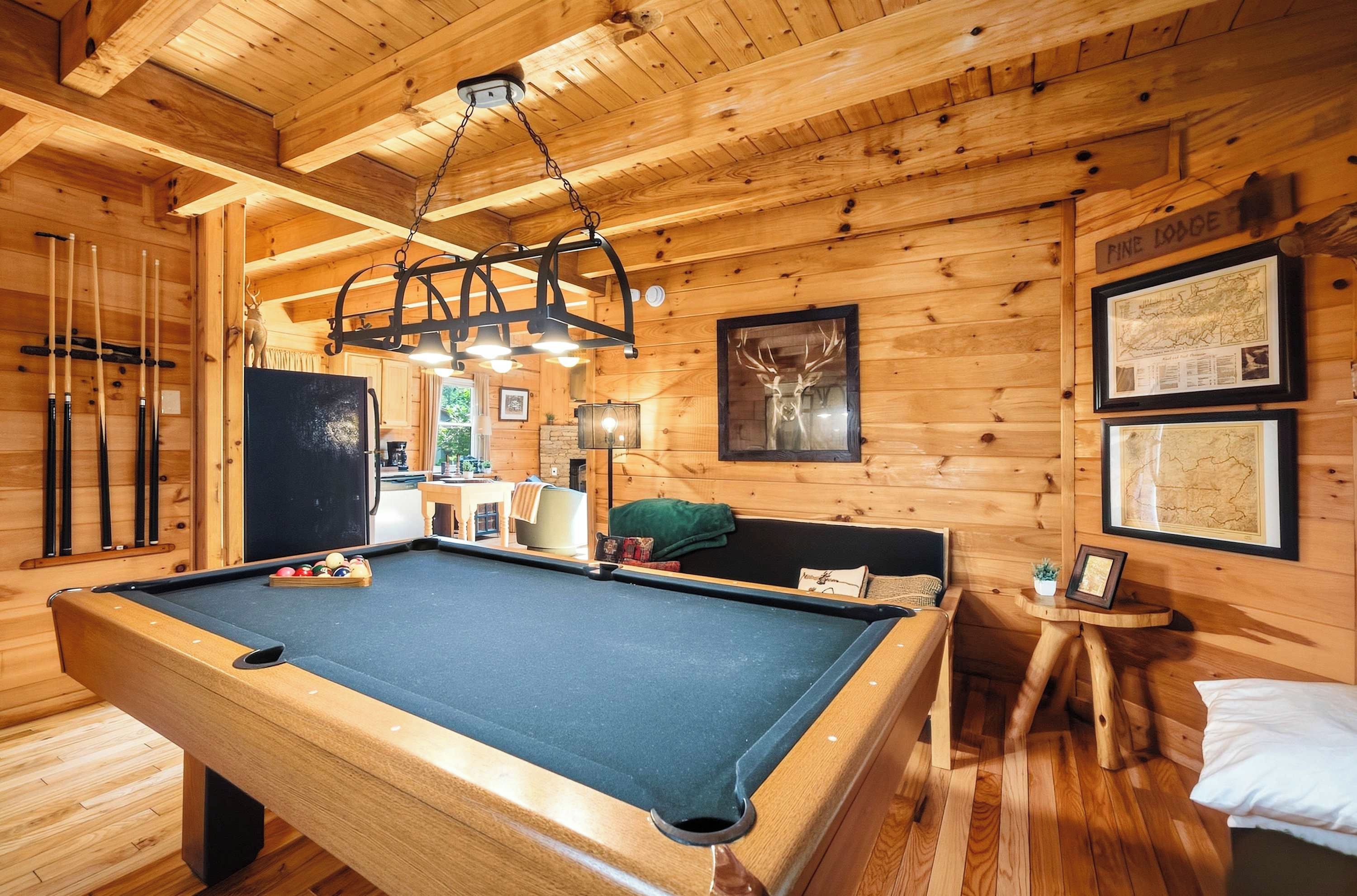 A wooden interior with a pool table, a ceiling light fixture, and framed maps on the wall.